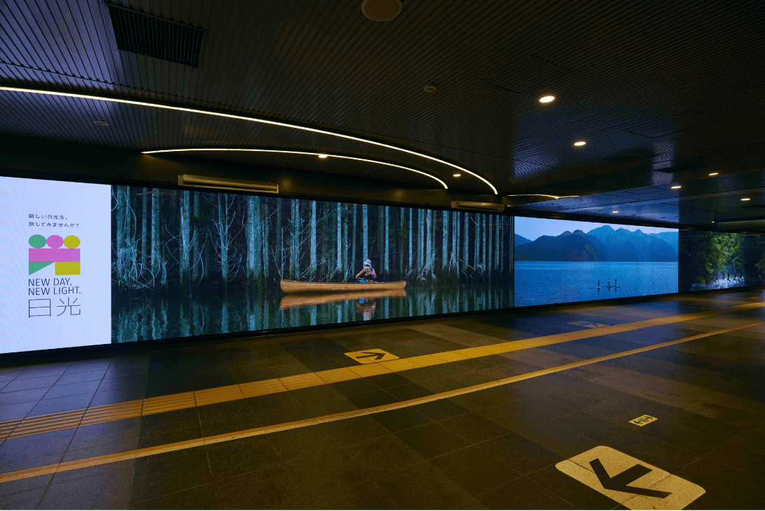 駅のホーム内に「NEW DAY, NEW LIGHT. 日光」プロジェクトのスクリーン映し出された湖に浮かぶボートの写真