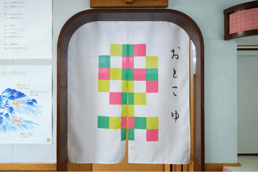 黄色、緑、ピンクの四角が集まって「男」の文字を表現し、その右横に「おとこゆ」と書かれた暖簾の写真