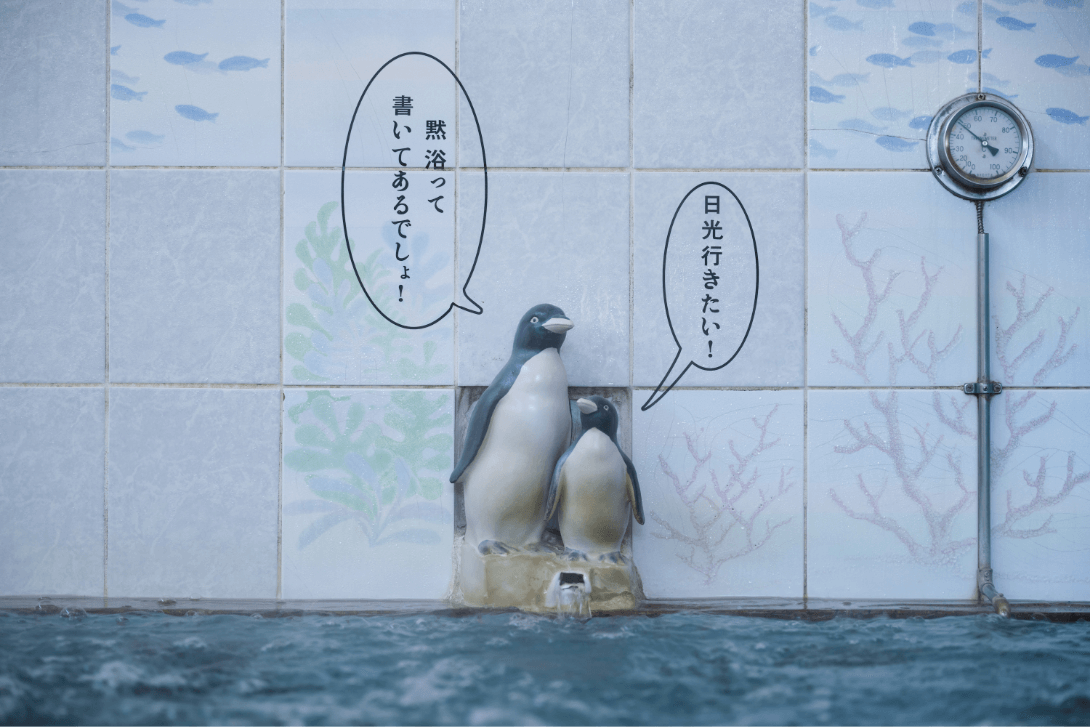 温泉のお湯の吹き出し口の上でお母さんペンギンが「黙浴って書いてあるでしょ！」子供ペンギンが「日光いきたい！」と言っているペンギン親子の人形の写真