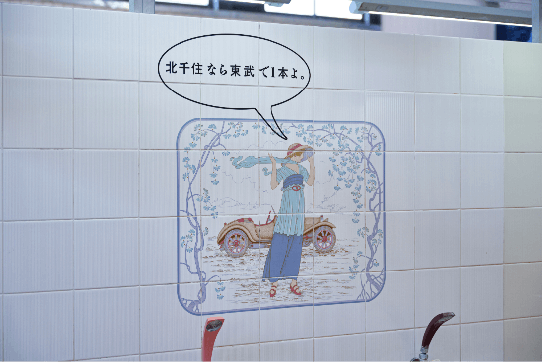 銭湯内の壁のタイルに「北千里なら東武で1本よ。」の文字と女性のイラストが描かれた写真