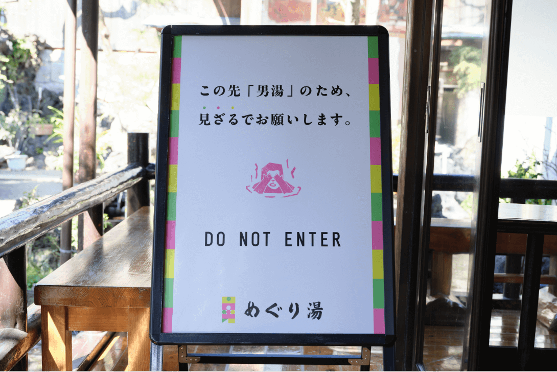 「この先「男湯」のため、見ざるでお願いします。」「DO NOT ENTER」の文字と、両手で目を隠している猿のイラストが描かれた看板の写真