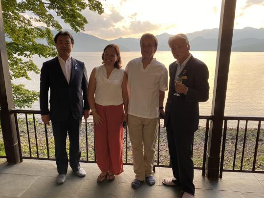 後方の中禅寺湖畔が太陽に照らされ、女性ベルギー大使と市長関係者4人で記念撮影をしている様子を写した写真