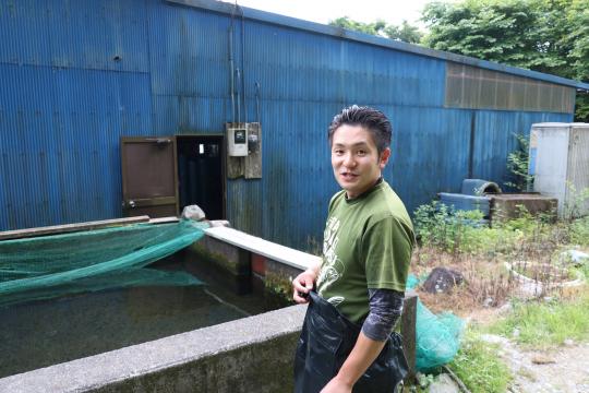 マスの養殖する水槽の前に立っている神山勇人さんの写真
