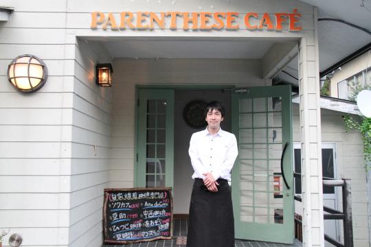 PARENTHESE CAFÉのエントランス前に立つ黒いエプロンを着た男性の写真