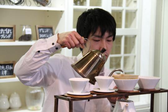 真剣なまなざしでコーヒーポットからコーヒーメーカーにコーヒーを注いでいる男性の写真