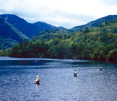 木々が生い茂る山を背景に湖で釣りをする人達の写真