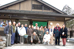 木造建ての「たくみ庵」の前で2列に並び記念撮影をしている参加者の写真