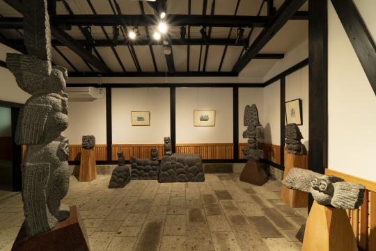 床が石畳の室内の壁に沿って置かれている、複数のフクロウの石像などの写真