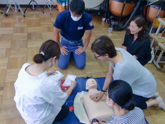 4人の男女が人形を使って心臓マッサージの訓練をしている写真