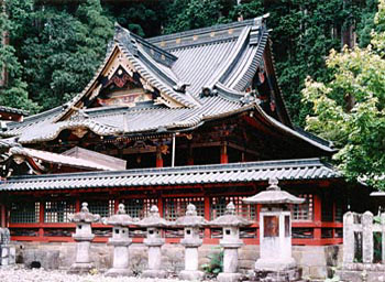 横一列に並んでいる複数の石灯籠と屋根付きの塀の奥に見えている二荒山神社本殿の写真