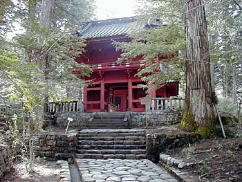 石畳の参道の先の階段の奥に周りを木々で囲まれて建っている全体が朱色をした二荒山神社別宮滝尾神社楼門の写真