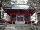 周りを木々で囲まれ、石階段の先に建っている入毋屋造、全体が朱色で扉部分が黒色の二荒山神社-別宮本宮神社拝殿の写真