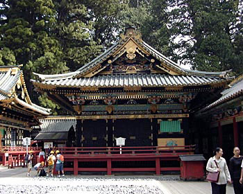 背景に大きな木が見える場所に建っている入母屋造、全体的に黒色、随所に金色の装飾がされ、高欄が朱色の東照宮神楽殿の写真