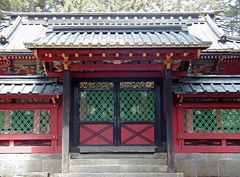 石階段の上に、黒い柱で屋根が支えられ、門の扉上半分が緑色の菱格子になっている仮殿唐門を正面から写した写真