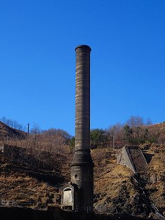 青い空を背景に立っている本山製錬所跡大煙突の写真