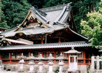 横一列に並んでいる複数の石灯籠と屋根付きの塀の奥に見えている二荒山神社本殿の写真