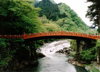 背景に山が見え、中央に流れる川の上に設置されている緩いアーチがかかった全体が朱色の二荒山神社神橋の写真