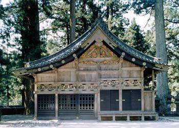 切妻造、シンプルな木造りで壁に彫刻が施されている神厩を正面から写した写真