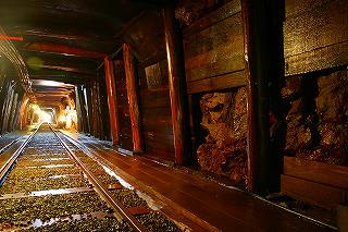 坑道内の天井や壁が木製の柱や板で補強され、地面には線路が敷かれている通洞坑坑道の写真