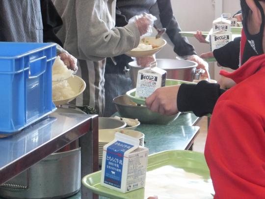 子どもたちが並んでいる給食の配膳で牛乳パックがトレイに置かれている写真