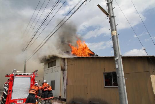 木造の建物から火と煙があがり、消防車を横付けし消防隊員の方々が消火しようとしている写真